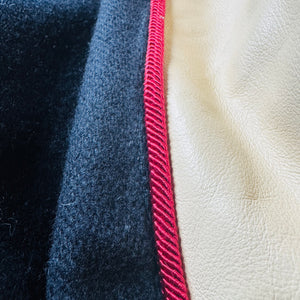 Close-up of a textile or leather material sample with three vertical sections: a dark navy fuzzy fabric, a dark blue textured fabric, and a light beige pebbled leather surface separated by a bright red stitched border.
