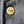 A round gold-tone metal pin with the words 'WORLD STUSSY TRIBE' in raised lettering, placed on a dark textured fabric background.