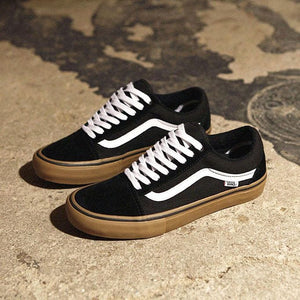 Black Vans Old Skool sneakers with white side stripe and gum sole, paired on textured surface